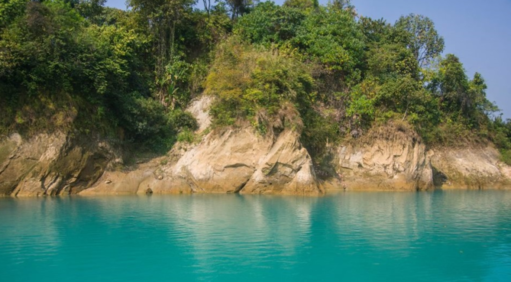 A scenic view of a lake with bright turquoise water, perfect for a travel for students getaway, surrounded by rocky cliffs and lush green trees under a clear blue sky.